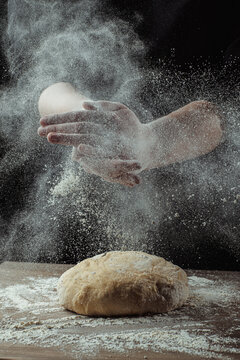 Baker clapping flour-covered hands above homemade bread dough on rustic wooden table