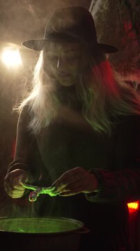 A witch brews a potion in a cauldron among dried herbs and cobwebs in an authentic home setting. She holds a voodoo doll over a cauldron with a potion and reads a spell