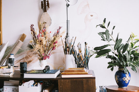 Dried flowers and paintbrushes stand in jars on a cabinet in a bright home art studio. Authentic small business concept for local creative art classes.