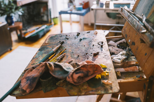 A wooden palette with mixed colorful oil paints rests on an easel in an art studio. Authentic local small business concept for painting art classes.