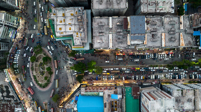 Aerial view of a busy urban intersection and roundabout with dense traffic, cars, buses, and pedestrians navigating streets between buildings in Dhaka, Dhaka Division, Bangladesh.