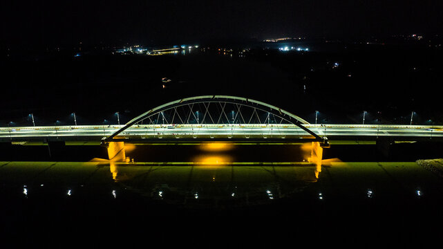 Aerial view of the illuminated arch bridge over the river at night, with bright lights reflecting on the water surface in Narail, Khulna Division, Bangladesh.