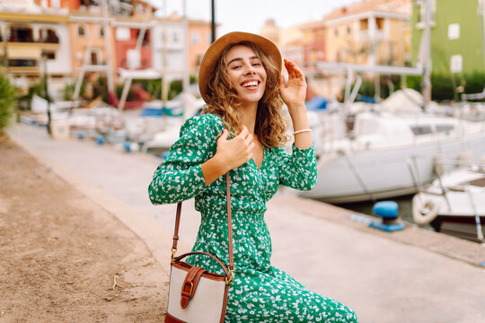 A happy woman strolls along the harbor path at sunset. The woman, wearing a dress and a hat, enjoys the moment outdoors. A concept of tourism and beauty.