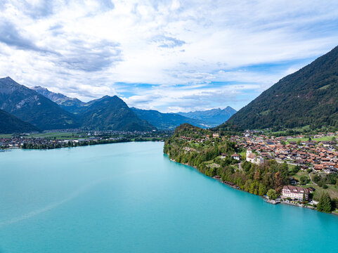 Aerial view of Lake Brienz and the village of Iseltwald nestled on the shore with lush green hills and mountains under a cloudy sky in Iseltwald, Canton of Bern, Switzerland.