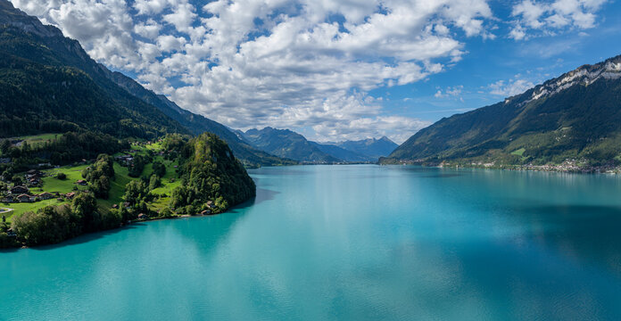 Aerial view of Lake Brienz with the village of Iseltwald nestled among green hills and mountains under a bright sky in Iseltwald, Canton of Bern, Switzerland.