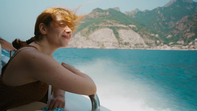 Smiling woman leaning on a boat railing with cliffs behind her Amalfi coast
