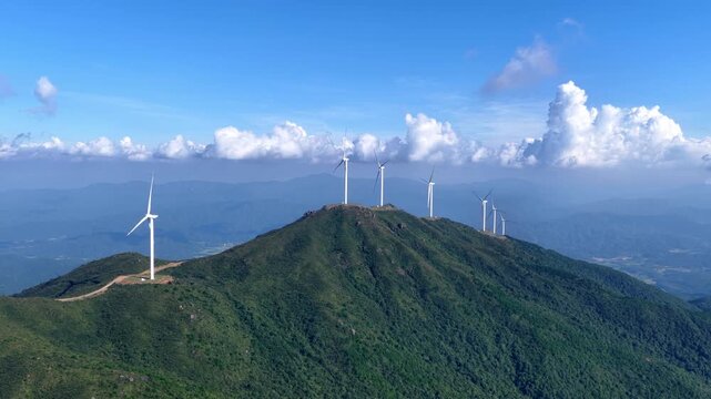 Wind turbines standing on the green mountain peak under blue sky
