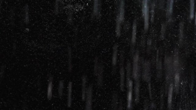 Tiny snow or dust randomly flying in the smoky air, empty space template for objects advertisement. Many dust particles cloud of white powder in low light on empty dark black contrast background.