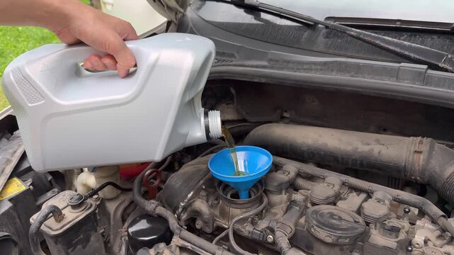 Hands placing plastic canister near engine hood for oil refill process.