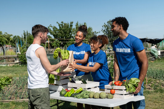 Volunteers are handing fresh vegetables and produce to a man at a community garden
