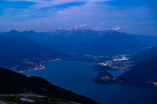 View of Lake Como at dusk, looking north from Santa Maria Rezzonico, featuring the Alps, towns, and mountains of the Valtellina.