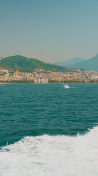 Coastal city skyline of Salerno behind the frothy wake of a departing ferry
