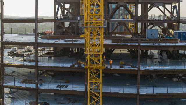 Aerial view of a high-rise building under construction featuring a yellow tower crane and steel framework with workers in high-visibility vests in Cambridge, Massachusetts, United States.