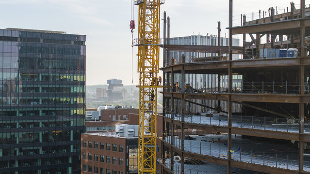 Aerial view of a construction site with a yellow tower crane and steel framework of a building under construction beside a modern glass building in Cambridge, Massachusetts, United States.