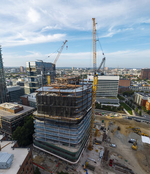 Aerial view of a large construction site with a high-rise building under development, featuring tall yellow cranes and steel framework in Cambridge, Massachusetts, United States.