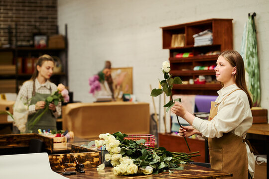 Young Caucasian female florists arranging fresh roses in flower shop studio. Image suitable for small business marketing, floristry workshop promotion, floral design advertising