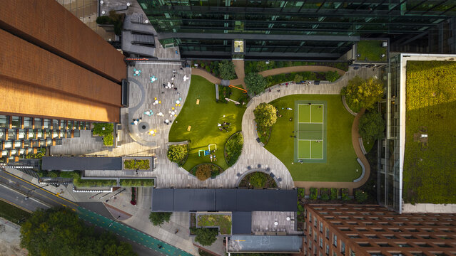Aerial view of an urban courtyard featuring a pickleball court, green lawns, and outdoor seating areas surrounded by modern office buildings in Cambridge, Massachusetts, United States.
