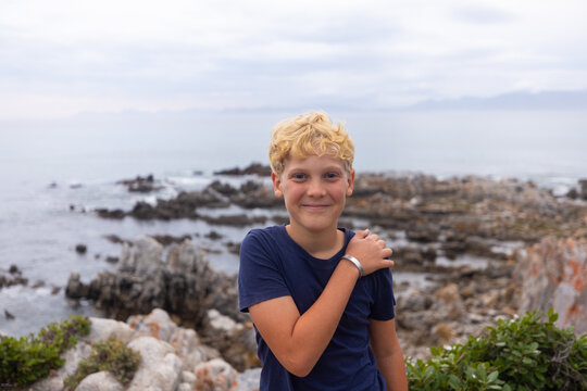 smiling boy in stormy late afternoon light on rocky coastline of DeKelders, South Africa