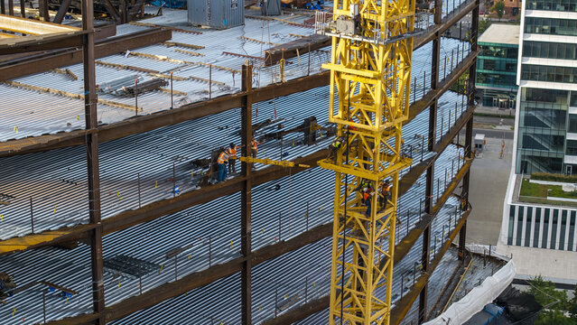 Aerial view of construction workers on the steel frame of a building under development with a large yellow tower crane in Cambridge, Massachusetts, United States.