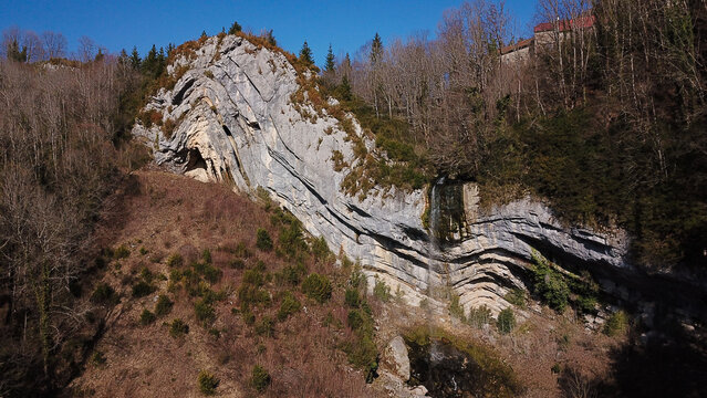 Aerial view of Gorges du Flumen featuring a waterfall cascading down a steep limestone cliff face surrounded by bare trees in Septmoncel les Molunes, Bourgogne-Franche-Comte, France.