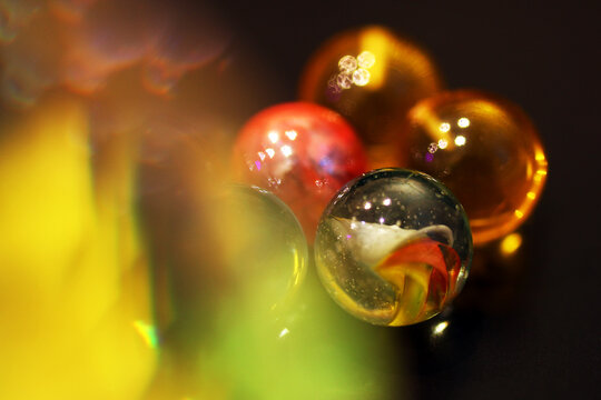 Colorful glass marbles in various shades, including green, red, and yellow, arranged on a dark surface. The marbles reflect light, creating vibrant display.