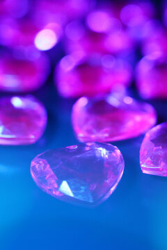 Close-up of sparkling purple heart-shaped gems on dark surface. The gems reflect light, creating a vibrant and colorful display.