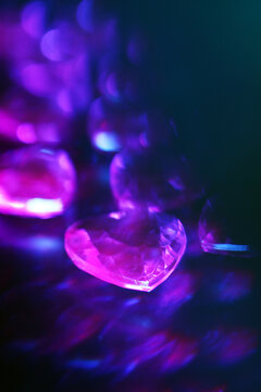 Close-up of sparkling purple heart-shaped crystals on a dark background. The crystals reflect light, creating vibrant and colorful display.