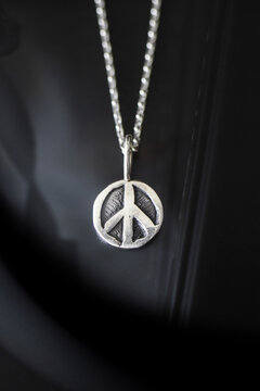 Silver peace symbol pendant hangs from a delicate chain. The background is softly blurred, emphasizing the pendant's design and shine.