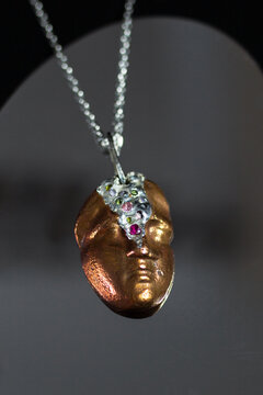 Close-up of a unique pendant featuring a bronze-colored face sculpture. The pendant is adorned with a silver chain and decorative elements.