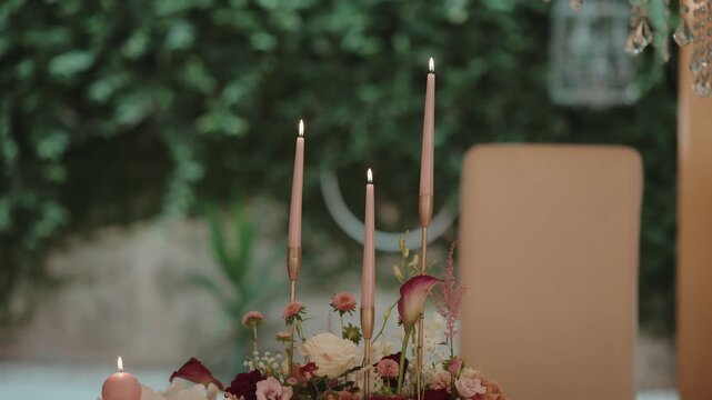 Table centerpiece featuring burning taper and round candles, surrounded by various fresh flowers, creating a warm, romantic atmosphere