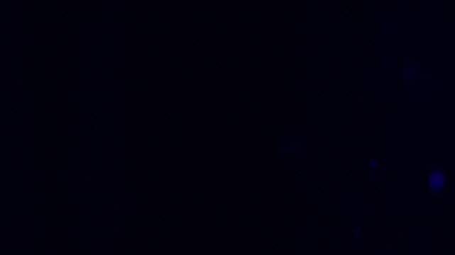 Tiny snow or dust randomly flying in the smoky air, empty space template for objects advertisement. Many dust particles cloud of white powder in blue light on empty dark black contrast background.