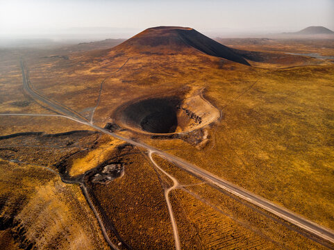 Aerial view of volcanic crater and cone near Lake Meke, surrounded by arid landscape and dry terrain with a road cutting through the volcanic field in Karapinar, Konya, Turkiye.