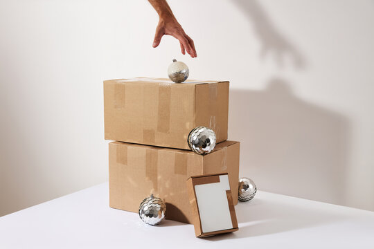 Hand Reaching for Christmas Ornament on Stacked Cardboard Delivery Boxes