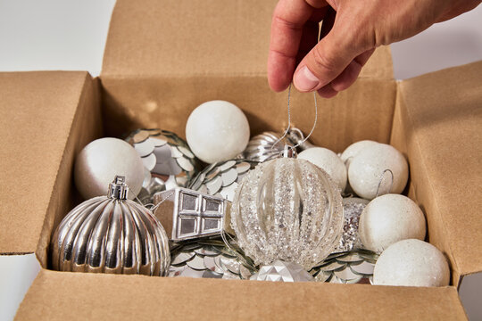 Hand Taking Christmas Tree Ornaments and Silver Baubles from Cardboard Box