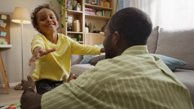 Cheerful African American child running into arms of sitting father and embracing him tightly. Perfect for fatherhood campaigns, family insurance ads and parenting projects