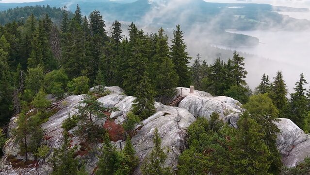 Aerial view of the rocky Ukko-Koli summit surrounded by dense pine forests and mist with a lake in the background in Koli, Pohjois-Karjala, Finland.