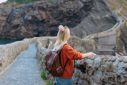Woman traveler with backpack exploring winding stone path at gaztelugatxe, spain, enjoy coastal scenery and hiking adventure.Beautiful scenic landscape of Dragonstone Game of Thrones filming location