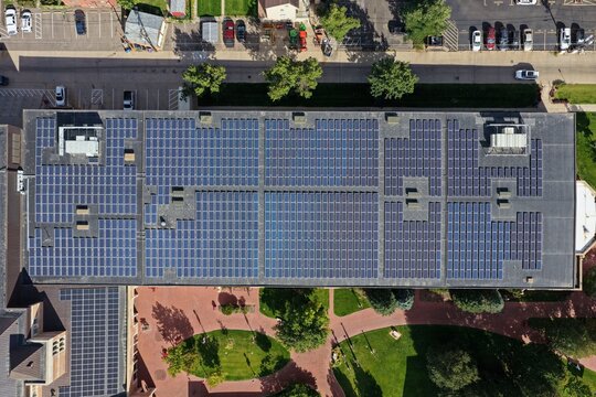 Aerial view of a large flat roof covered in solar panels with surrounding parking lot and green space in Denver, Colorado, United States.