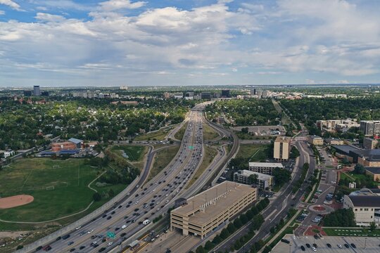 Aerial view of a busy highway interchange with heavy traffic surrounded by urban development, green parks, and a parking structure in Denver, Colorado, United States.