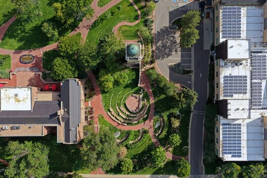 Aerial view of a park featuring a clock tower, curved stone seating, lush green lawns, and adjacent buildings with solar panels in Denver, Colorado, United States.