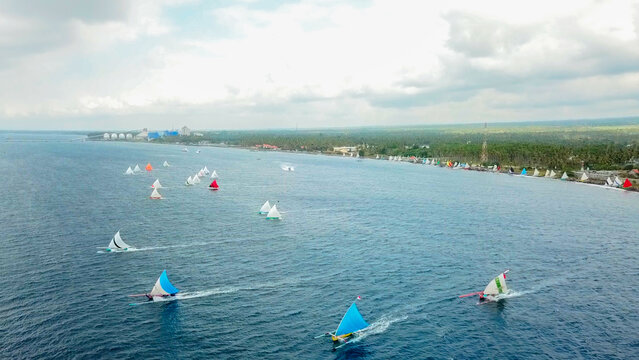 Aerial view of traditional sailing boats with colorful sails racing along the coastline of Indonesia.