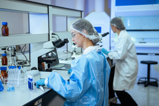 A team of researchers conducts medical tests and analyzes chemical samples using microscopes and lab equipment inside a clean laboratory facility during daytime work hours.