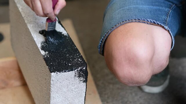 Man painting the edge of a concrete building block with black paint