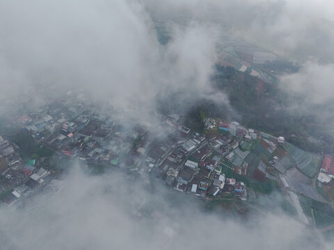 Aerial view of Nepal Van Java village nestled on the slopes of Mount Sumbing with terraced agricultural fields partially obscured by dense clouds in Magelang, Central Java, Indonesia.