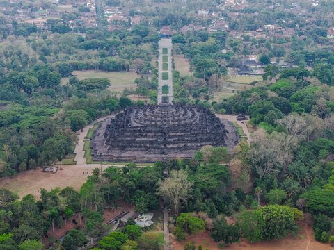 Aerial view of Borobudur Temple, an ancient Buddhist monument surrounded by lush tropical trees and greenery in Magelang, Jawa Tengah, Indonesia.