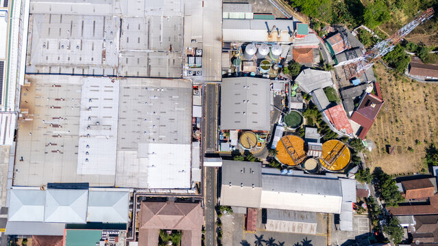 Aerial view of an industrial facility featuring large factory buildings, circular storage tanks, and surrounding vegetation in Salatiga, Central Java, Indonesia.