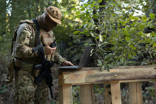 A soldier works on a laptop and a two-way radio in the field while carrying out a mission.