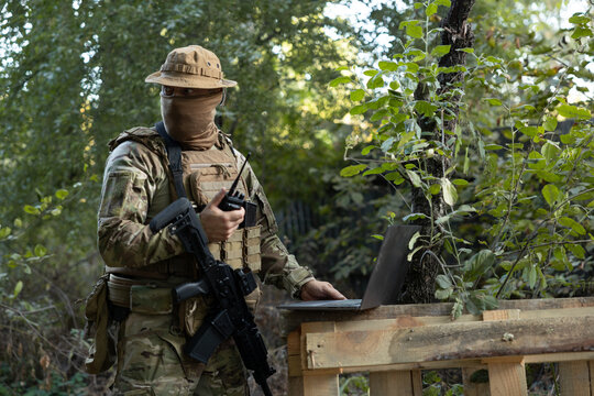 A soldier works on a laptop and a two-way radio in the field while carrying out a mission.