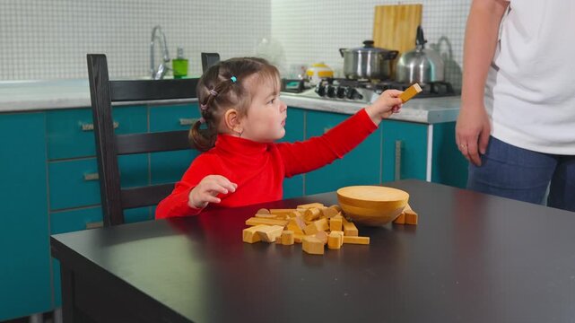 A young Caucasian mother plays with her little daughter using wooden blocks at a table at home. Their activity reflects Montessori education, family bonding, and early childhood development