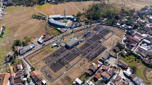 Aerial view of an electrical substation surrounded by residential houses, agricultural fields, and lush greenery in Salatiga, Central Java, Indonesia.